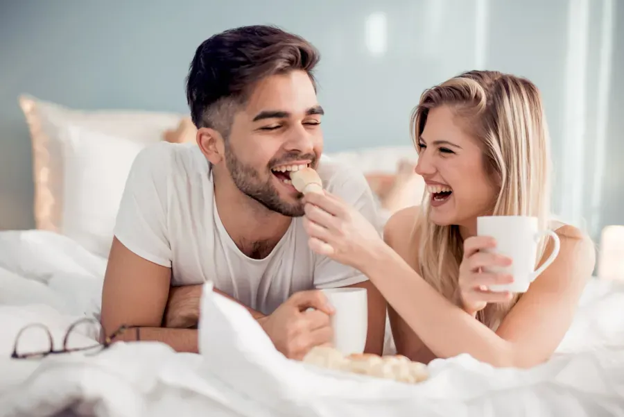Couple sharing morning coffee and breakfast in bed happily